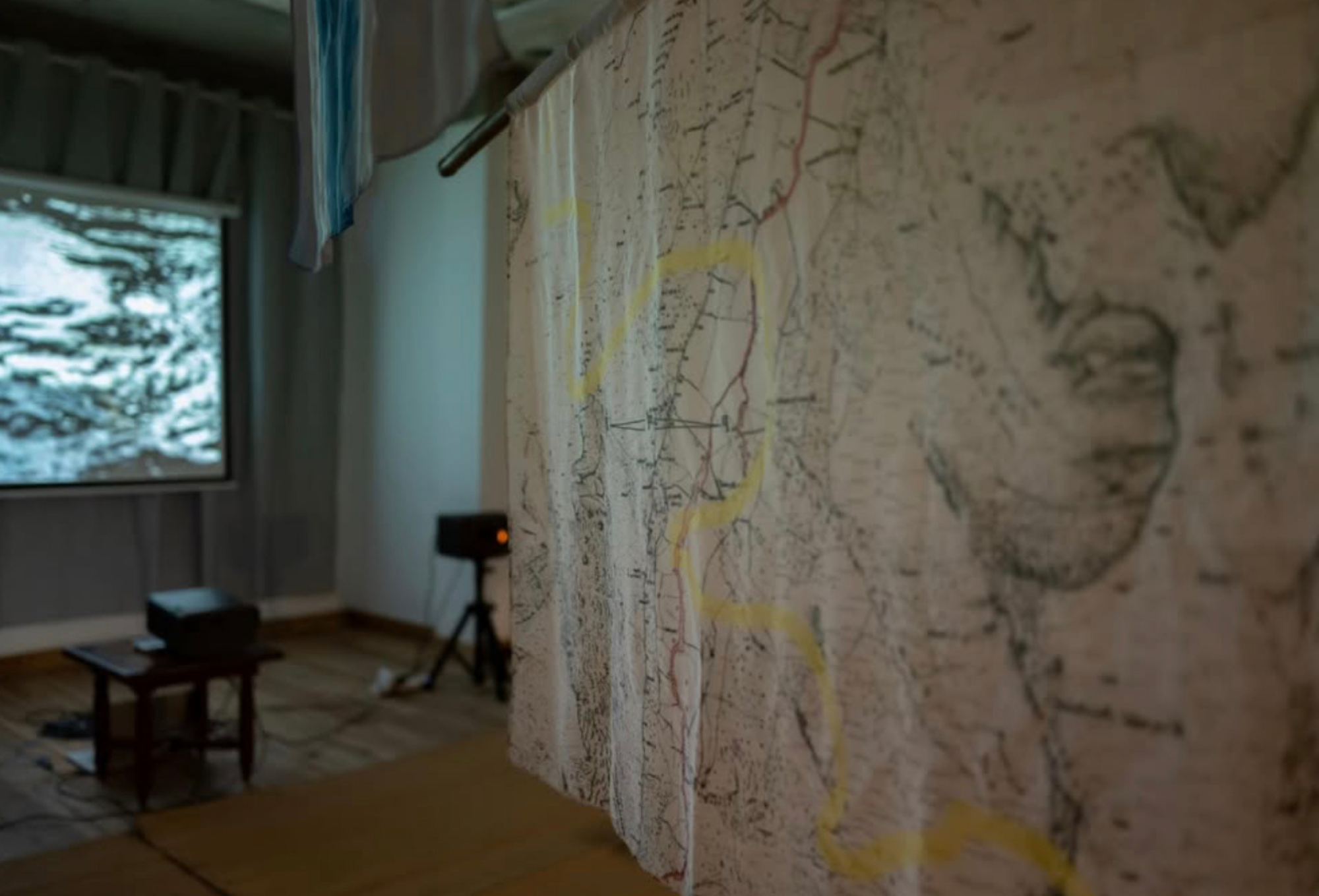 A large, hanging fabric map with a yellow line detail occupies the foreground, while a projector screen and equipment are visible in the background.